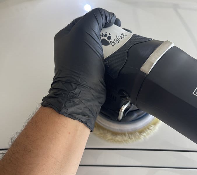 Professional paint correction in progress using machine polisher and inspection lighting